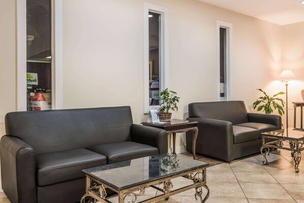A living room with two dark leather sofas, a glass coffee table, and a potted plant. - Baymont by Wyndham Lumberton NC (Lumberton)