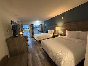 Habitación de hotel con dos camas, un escritorio, televisor y ventana con cortinas.