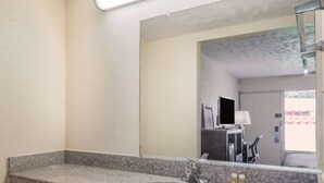 A bathroom with a granite countertop, a sink, a mirror, and a window with a view of buildings. - Baymont by Wyndham Lumberton NC (Lumberton)