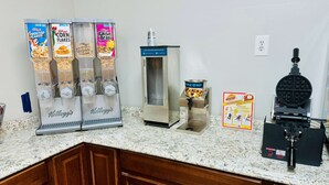 A breakfast bar with multiple cereal dispensers, a waffle maker, and a waffle iron. - Baymont by Wyndham Lumberton NC (Lumberton)