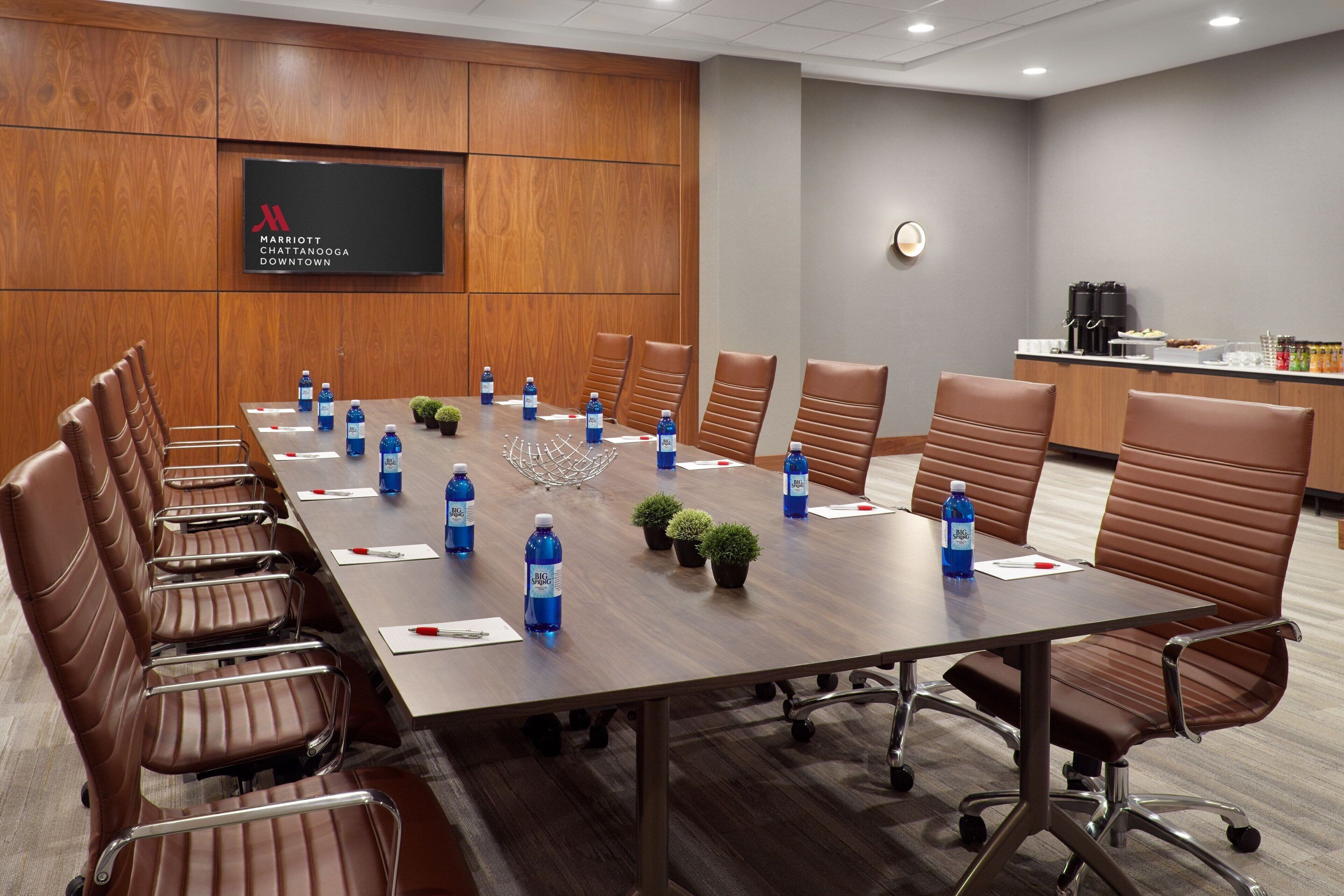 A conference room with a long table, brown leather chairs, water bottles, and a clock on the wall.