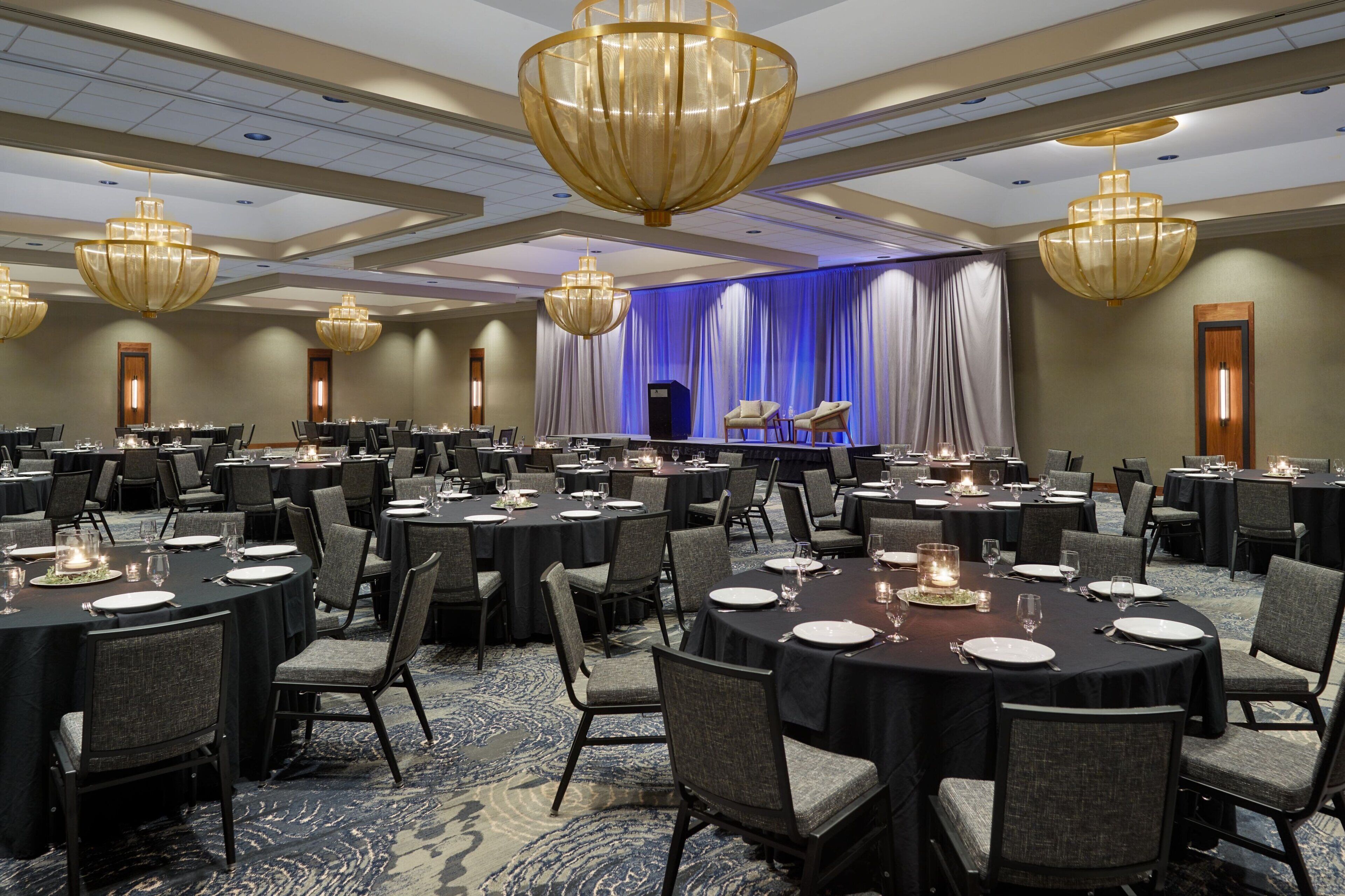 A banquet hall with round tables, chairs, and large chandeliers.