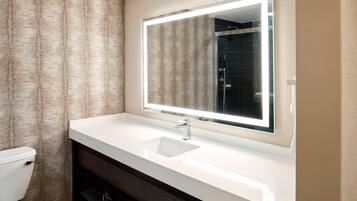 A bathroom with a white sink, a mirror with integrated lighting, a toilet, and a dark wooden cabinet.
