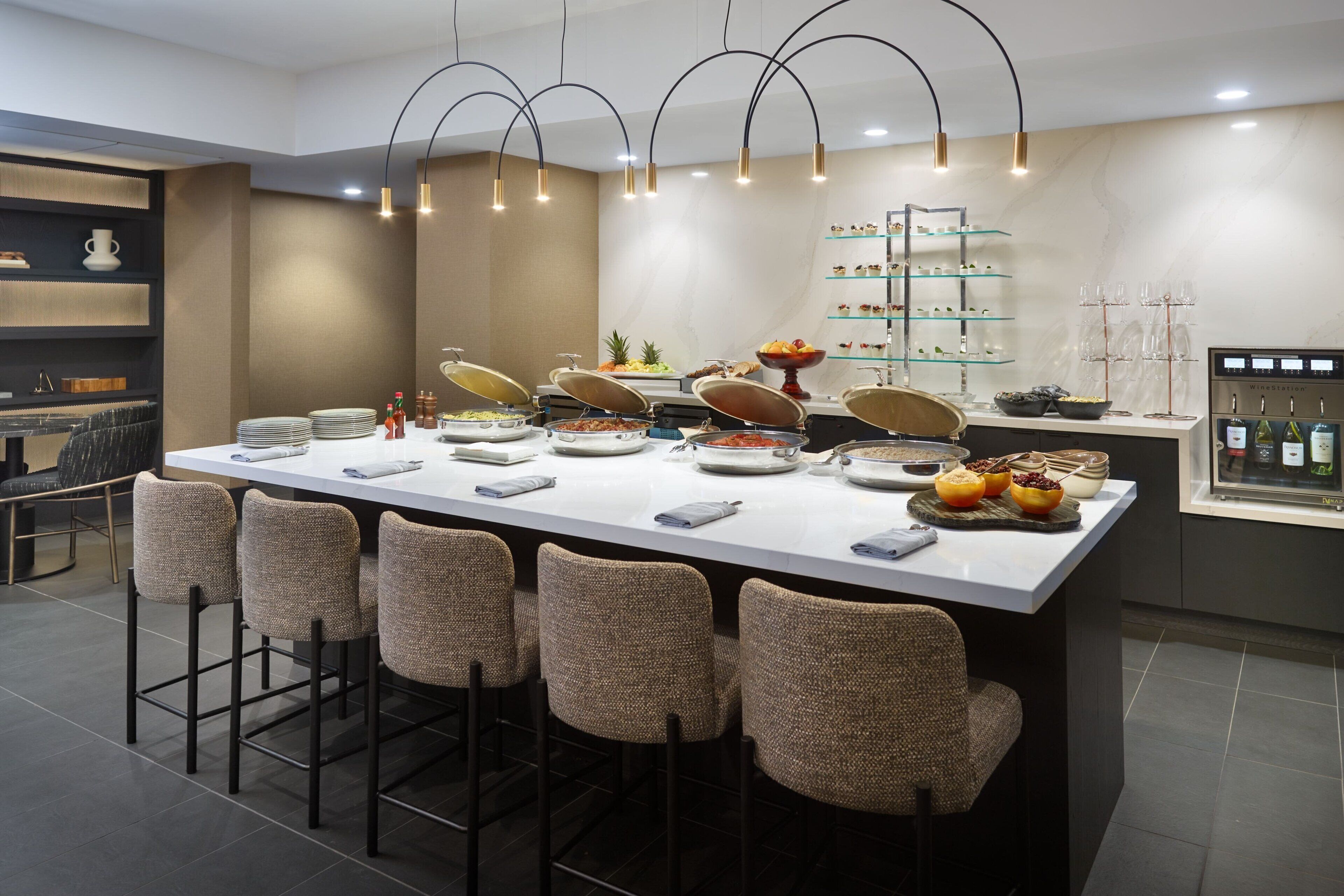 Zona de bar moderna con una barra larga, taburetes y diversas opciones de comida y bebida.