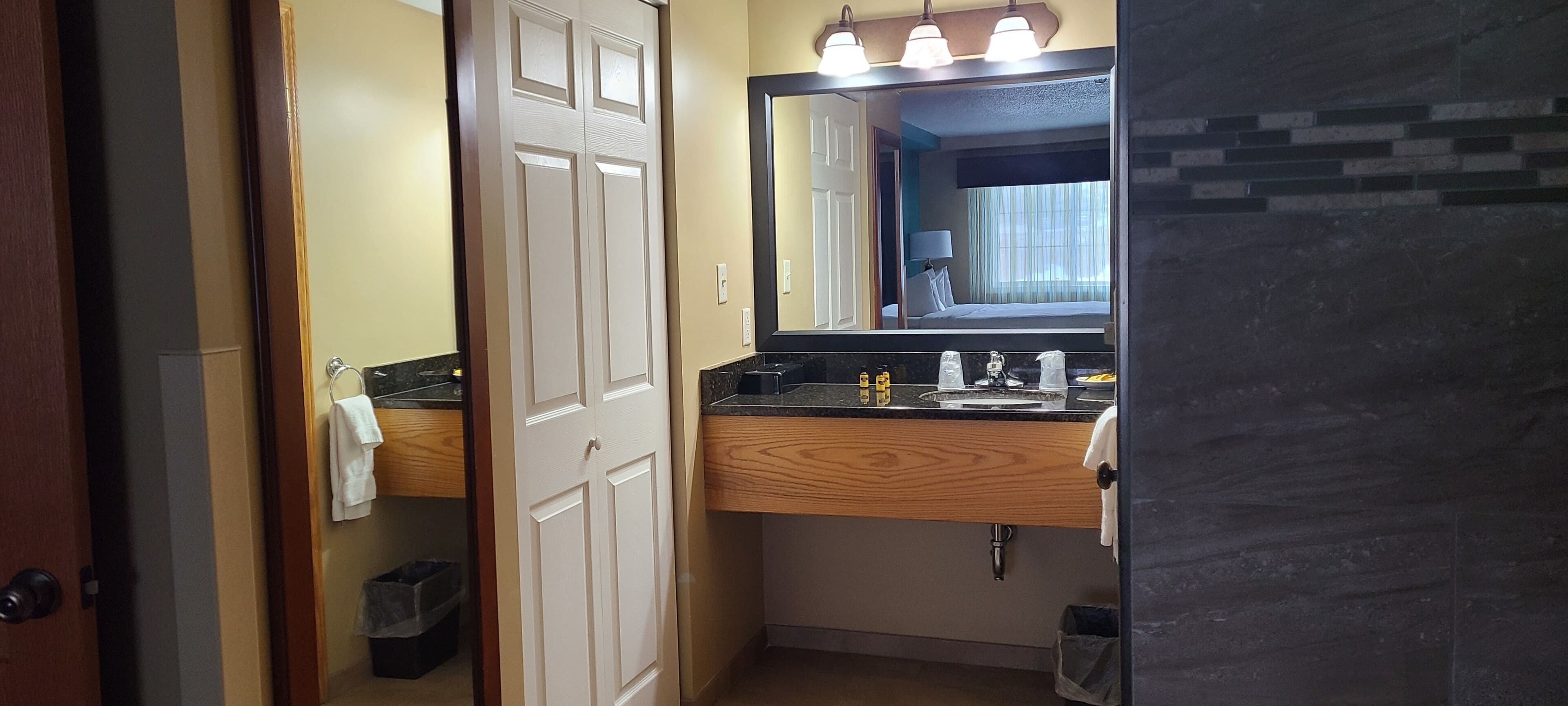 A bathroom with a wooden vanity, a mirror, and a sink. There is a door leading to another room.