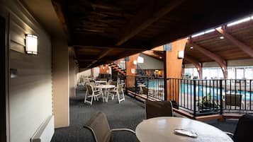 An indoor pool area with a wooden ceiling, tables, and chairs arranged for guests.
