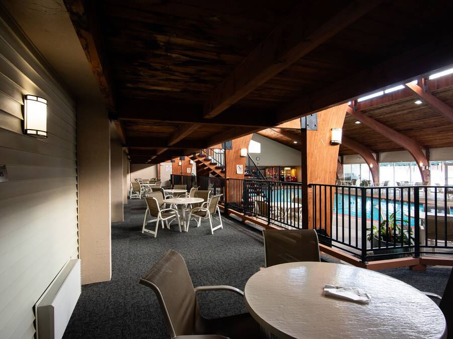 An indoor pool area with a wooden ceiling, tables, and chairs arranged for guests.