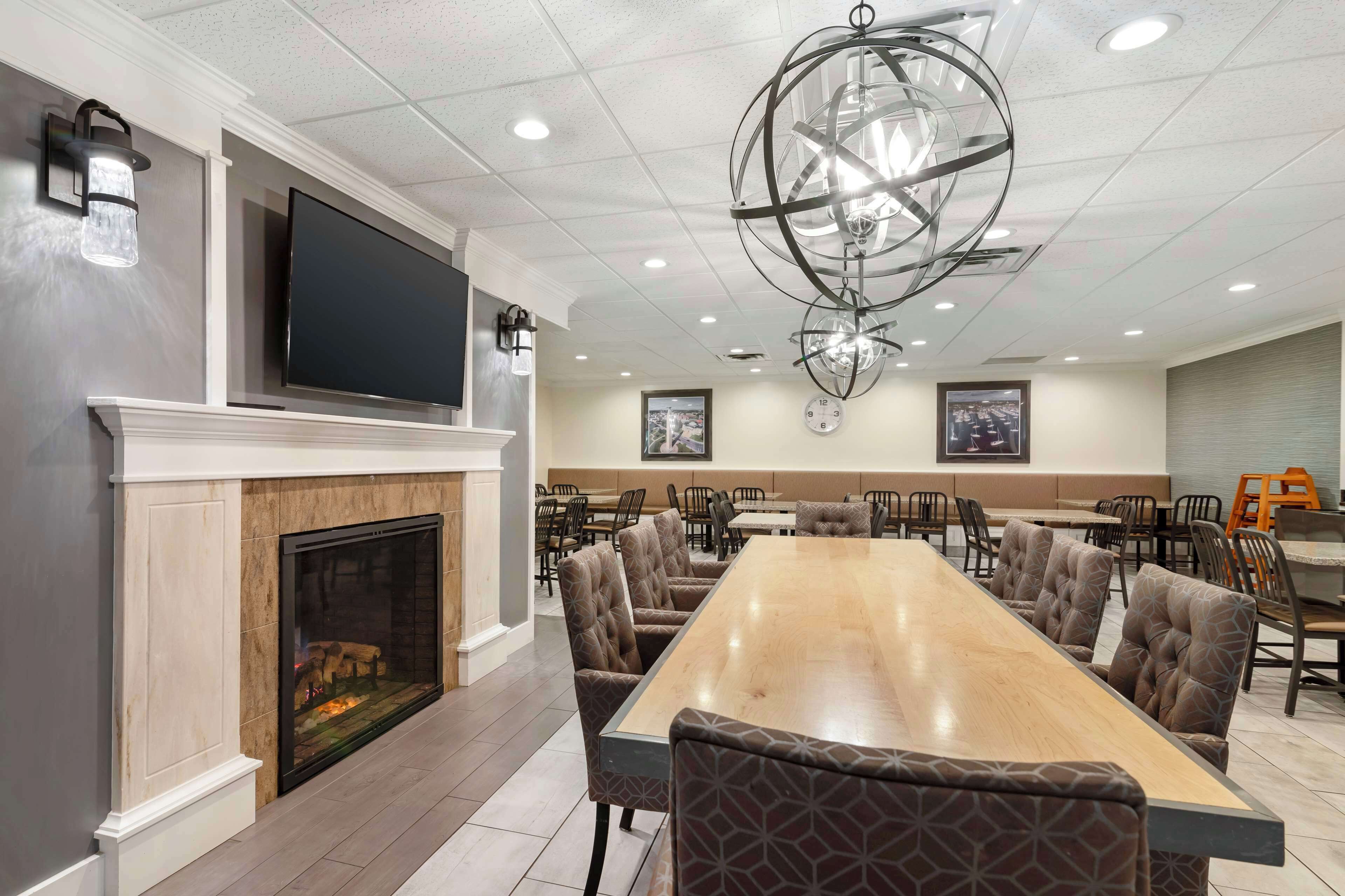 A spacious dining area with a long wooden table, comfortable upholstered chairs, a fireplace, and a large flat-screen TV mounted above.