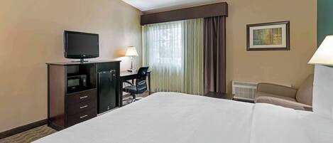 Une chambre d’hôtel dotée d’un grand lit, d’un téléviseur à écran plat, d’un bureau avec une chaise, d’une lampe, d’un tableau encadré au mur et d’un appareil de climatisation.