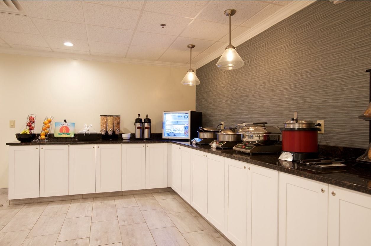 Una cocina moderna con armarios blancos, encimera negra y diversos electrodomésticos, incluyendo una cafetera, una cocedora de arroz y un tostador.