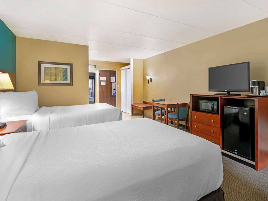 A hotel room with two beds, a desk with a chair, a television, a mini-fridge, and a microwave.