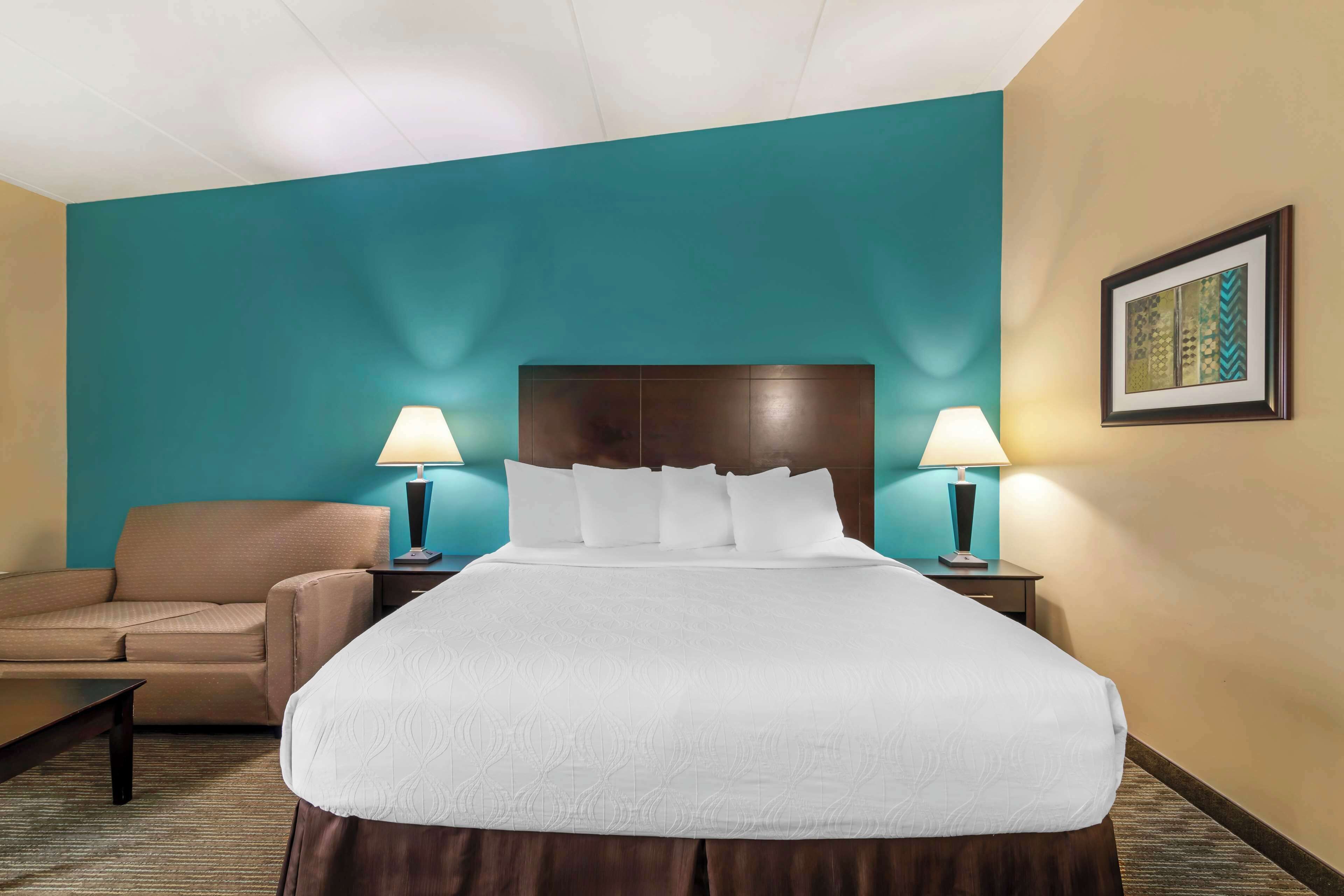 Una habitació d'hotel amb un llit gran, dues taules de nit amb làmpades, un sofà i un quadre al mur.