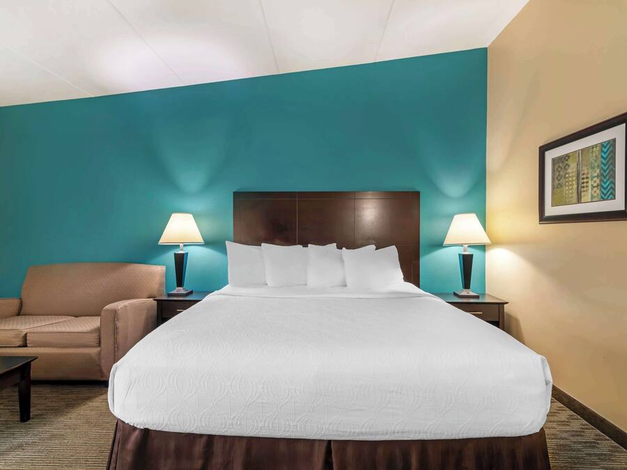 Una habitació d'hotel amb un llit gran, dues taules de nit amb làmpades, un sofà i un quadre al mur.