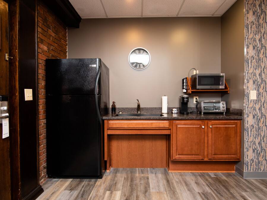 A compact kitchen with a black refrigerator, wooden cabinets, a microwave, and a sink.