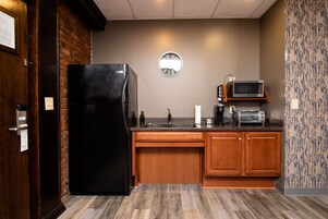 Una cocina compacta con un refrigerador negro, armarios de madera, un microondas y un lavamanos.
