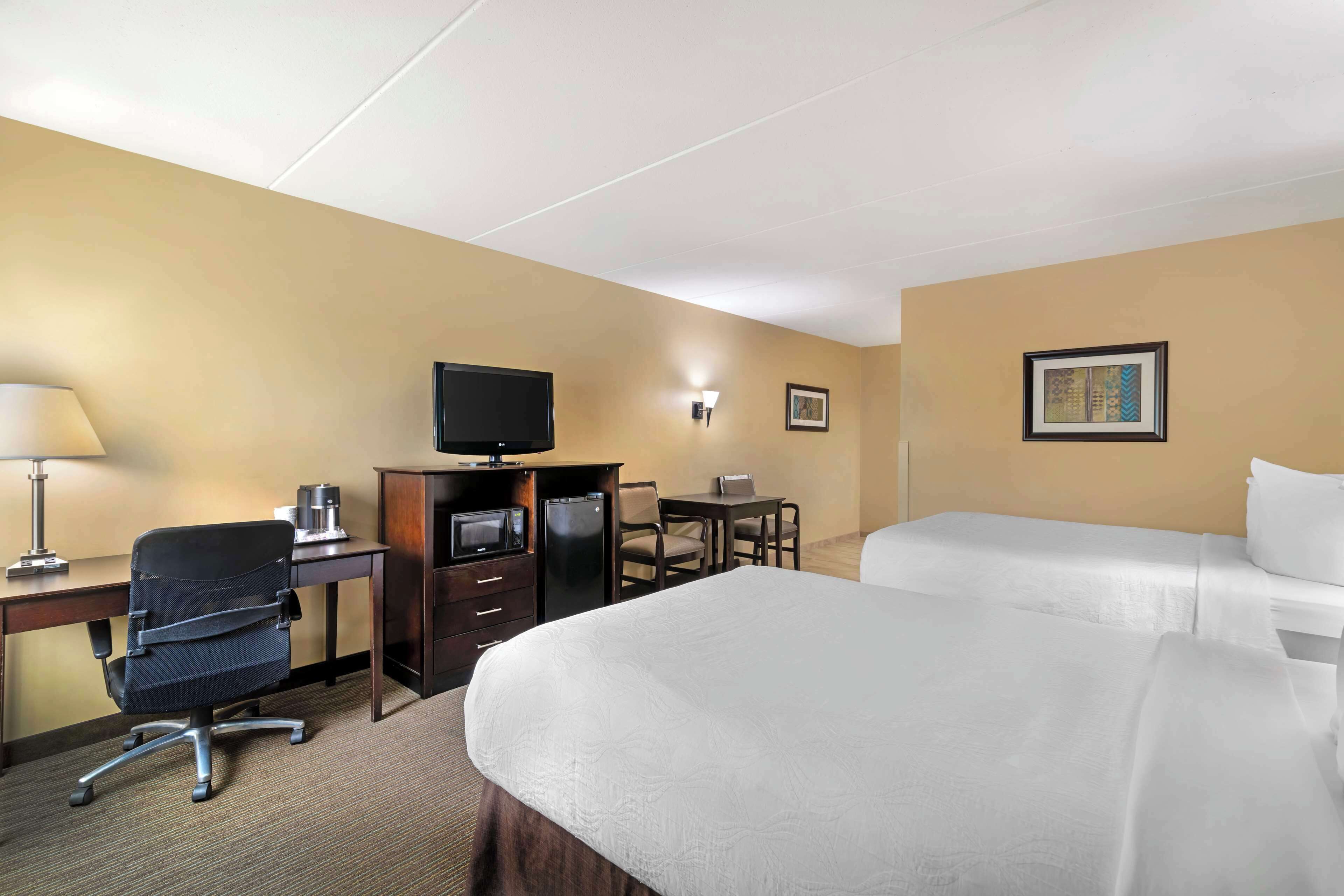A hotel room with a bed, a desk with a chair, a television, and a small table with chairs.