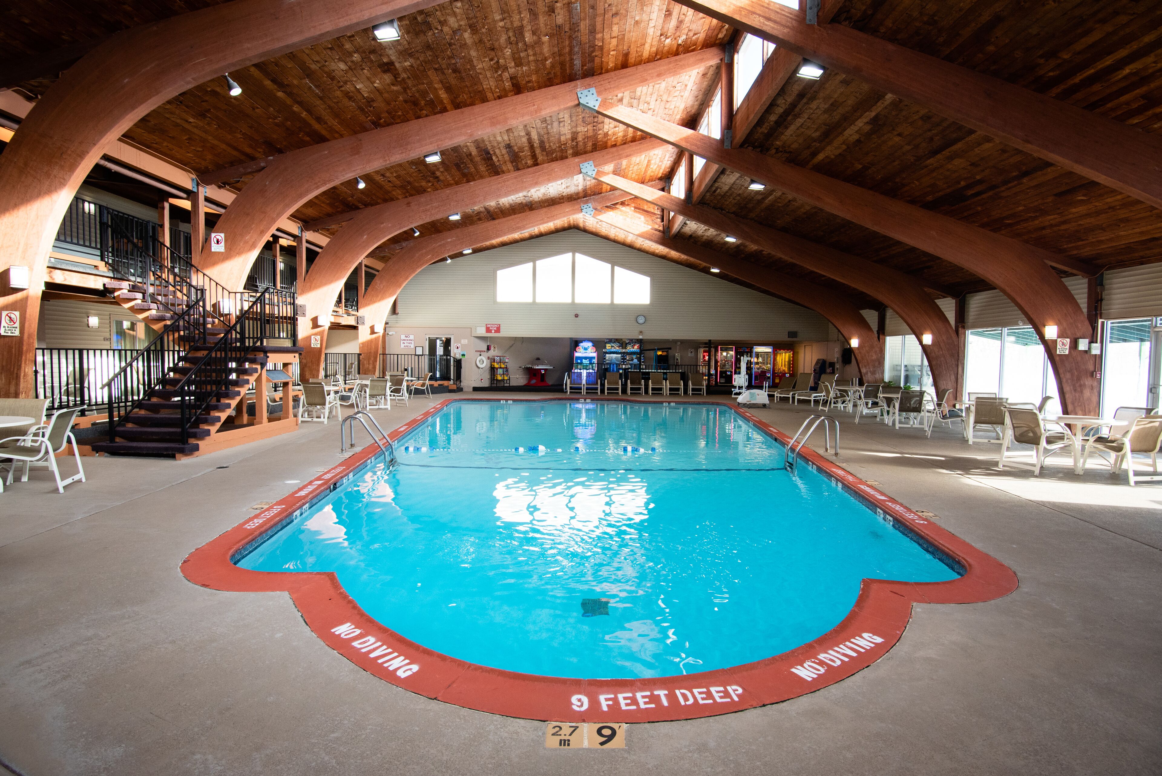 An indoor swimming pool with a wooden ceiling and a 9 feet deep sign at the edge.