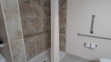 A bathroom with a shower area, grab bars, a toilet, and a towel rack.