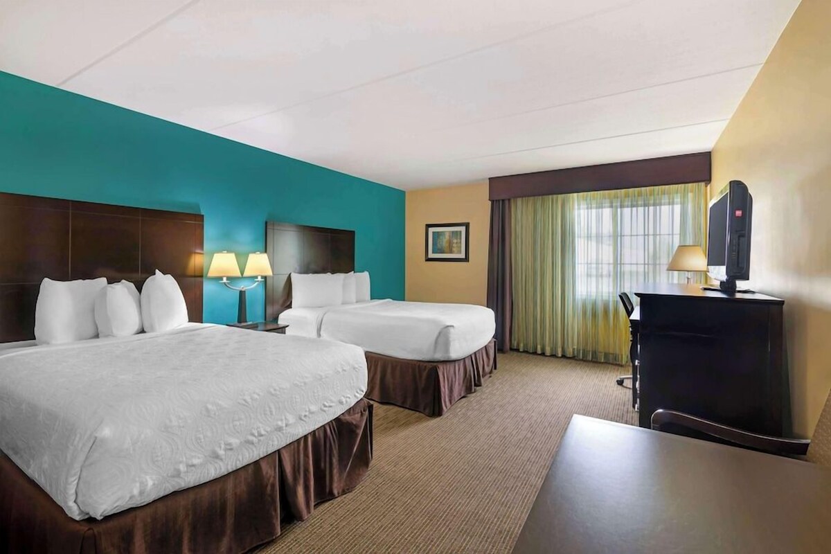 A hotel room with two beds, a desk, a dresser, and a window with curtains.