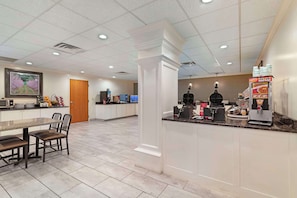 A modern kitchen area with a dining table, chairs, a coffee machine, and a food display.