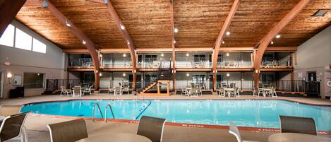 An indoor swimming pool with multiple levels of seating and a wooden ceiling.