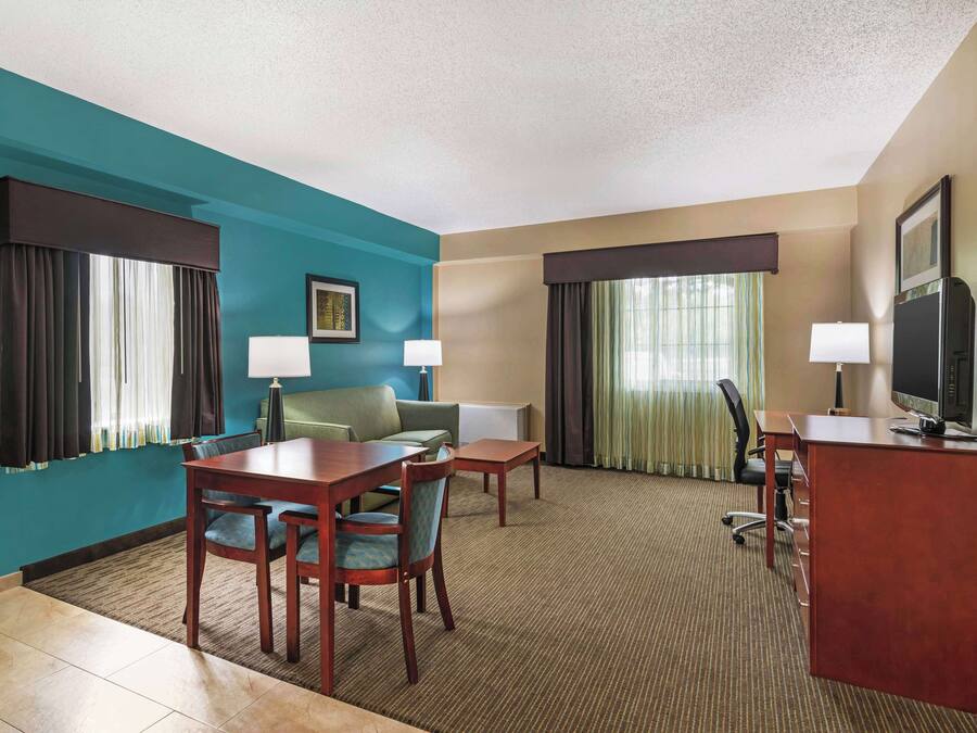 Habitación de hotel con paredes verde azuladas, un escritorio de madera, un sofá verde, un televisor y una ventana con cortinas.