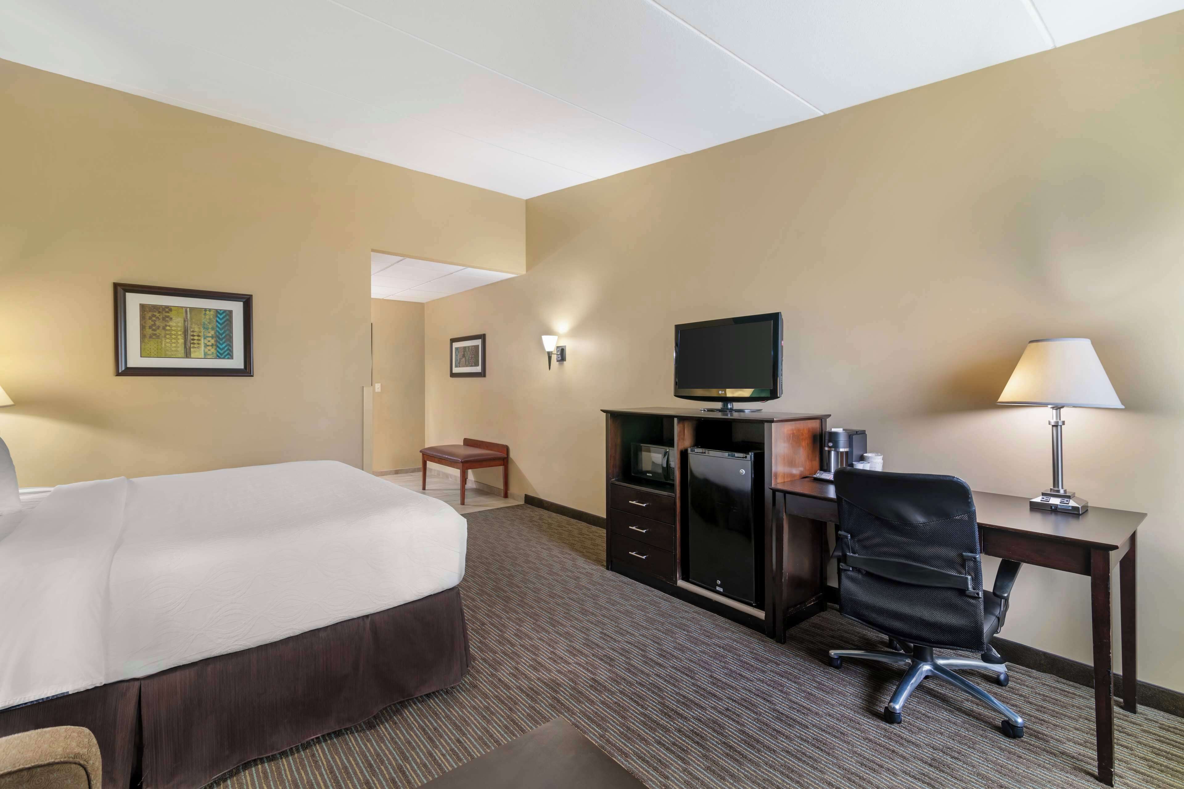 A hotel room with a bed, desk, chair, television, and wall-mounted lamp.