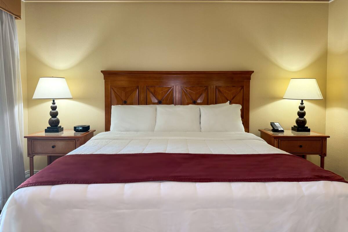 A hotel room with a large bed, two bedside tables with lamps, and a wooden headboard.