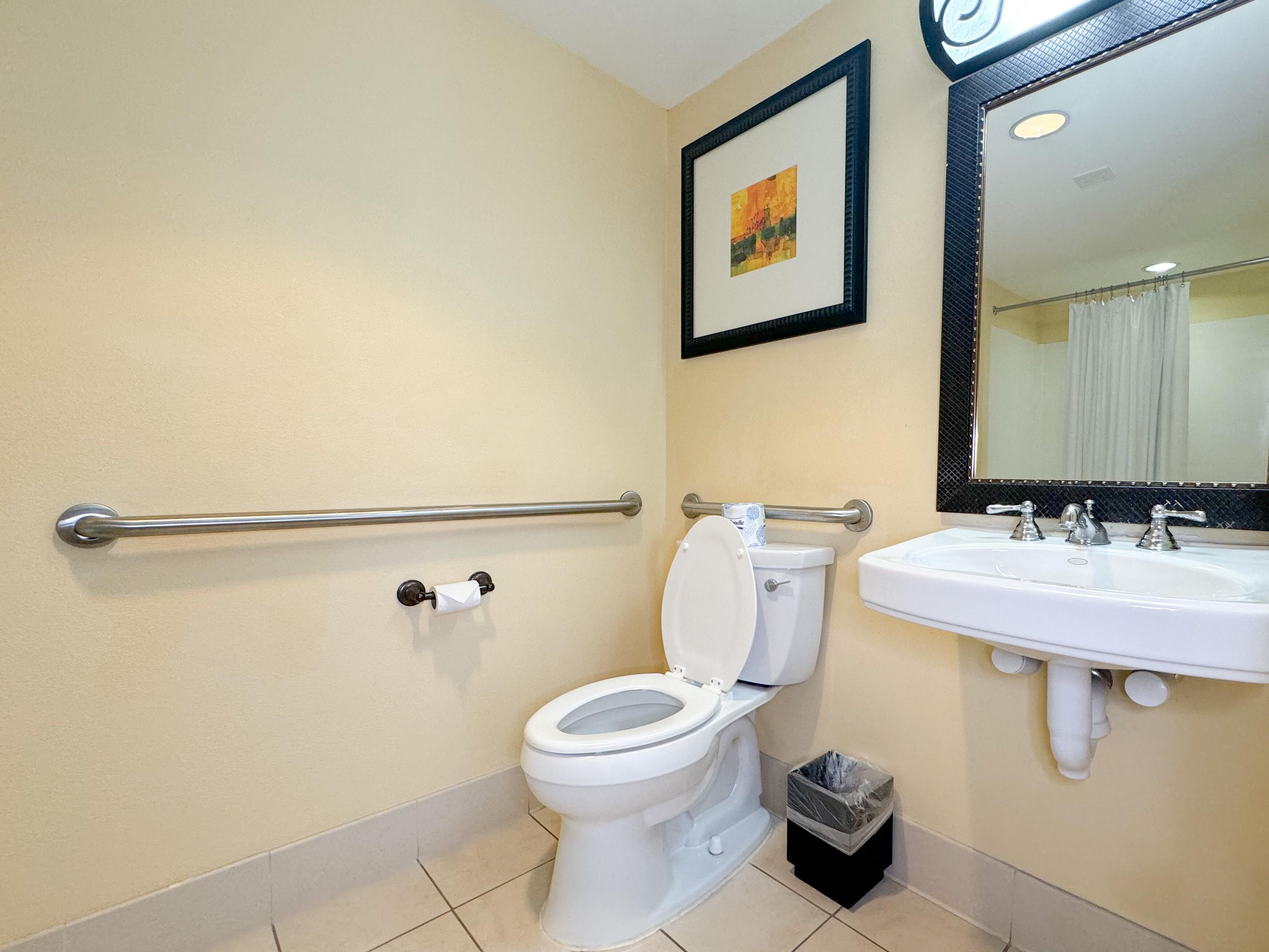 A bathroom with a toilet, sink, and handrail.