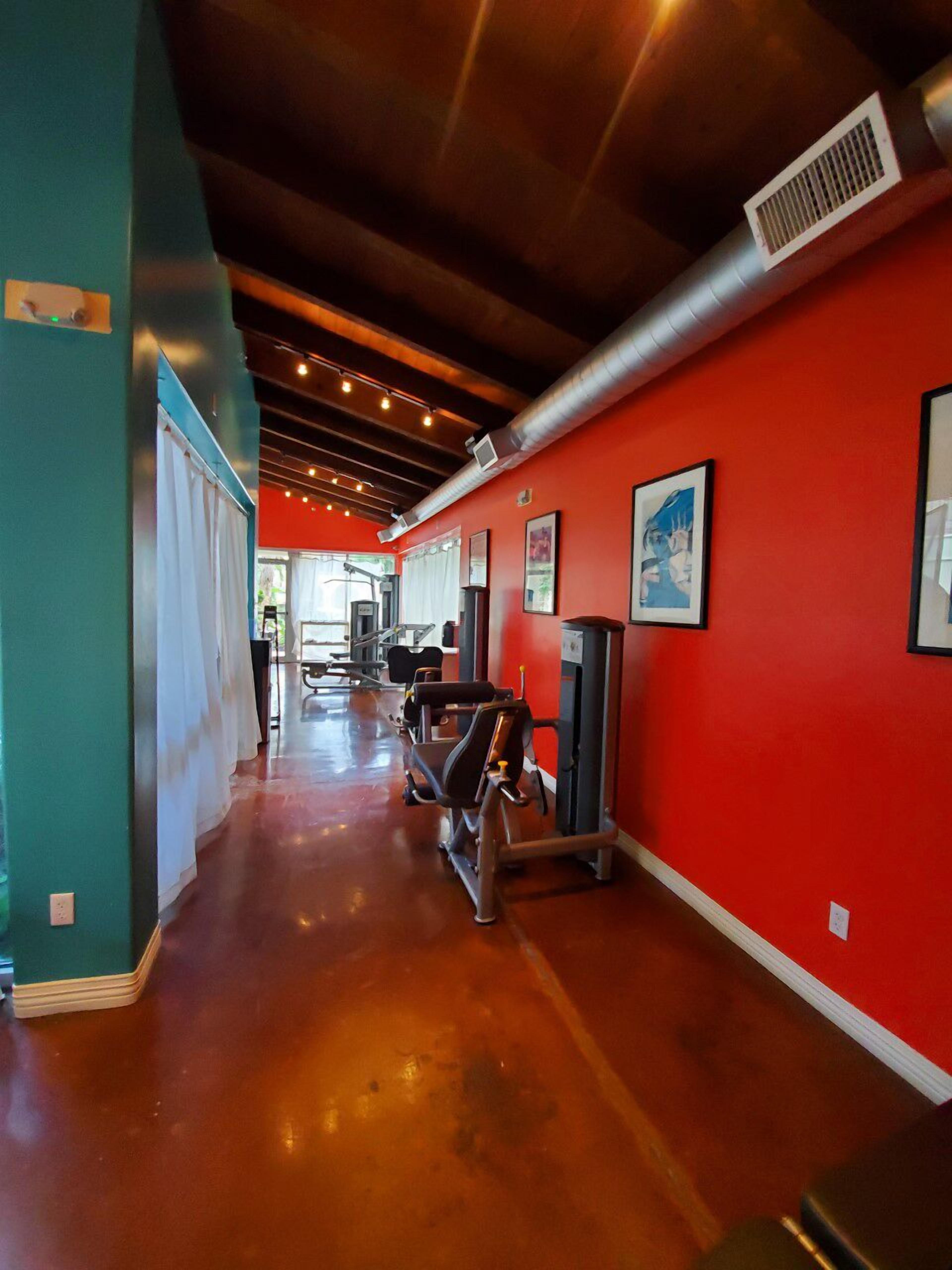 A gym with red walls, exercise equipment, and a polished concrete floor.