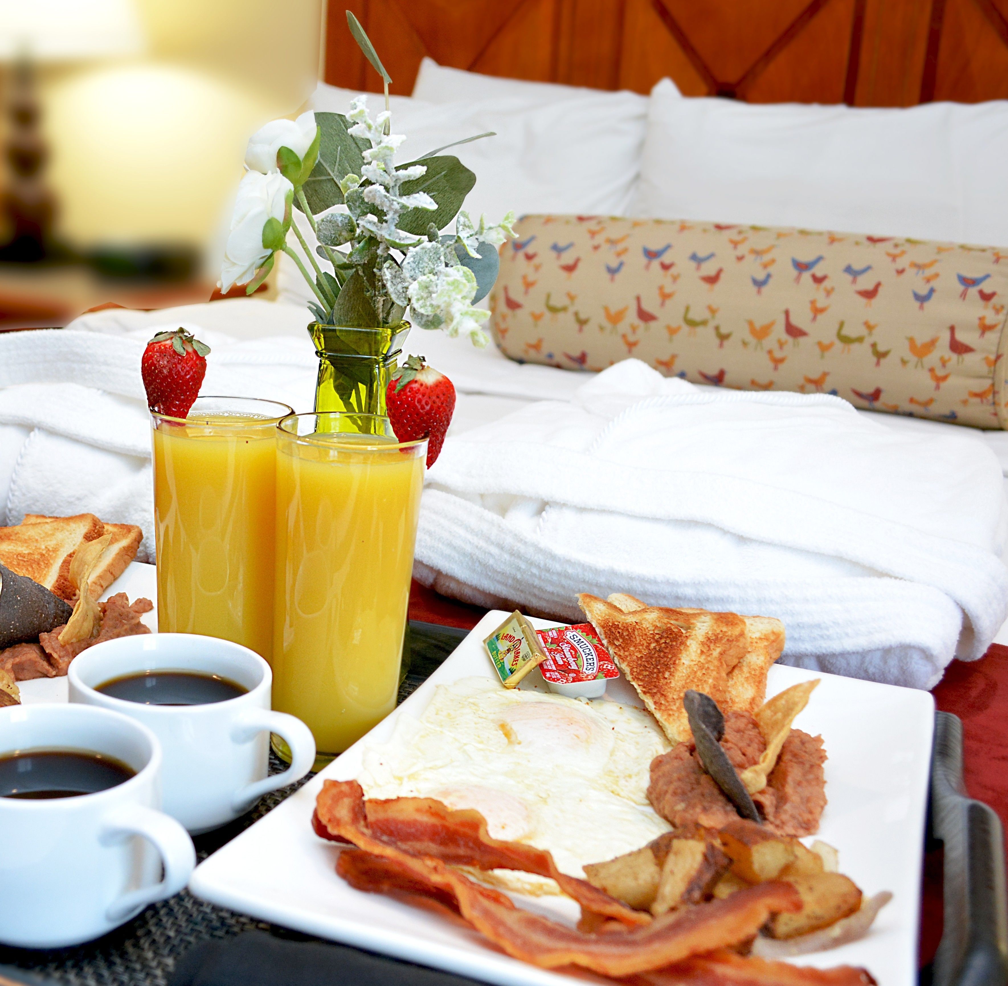 A breakfast setup with toast, bacon, eggs, and fruit on a tray, accompanied by coffee and orange juice.