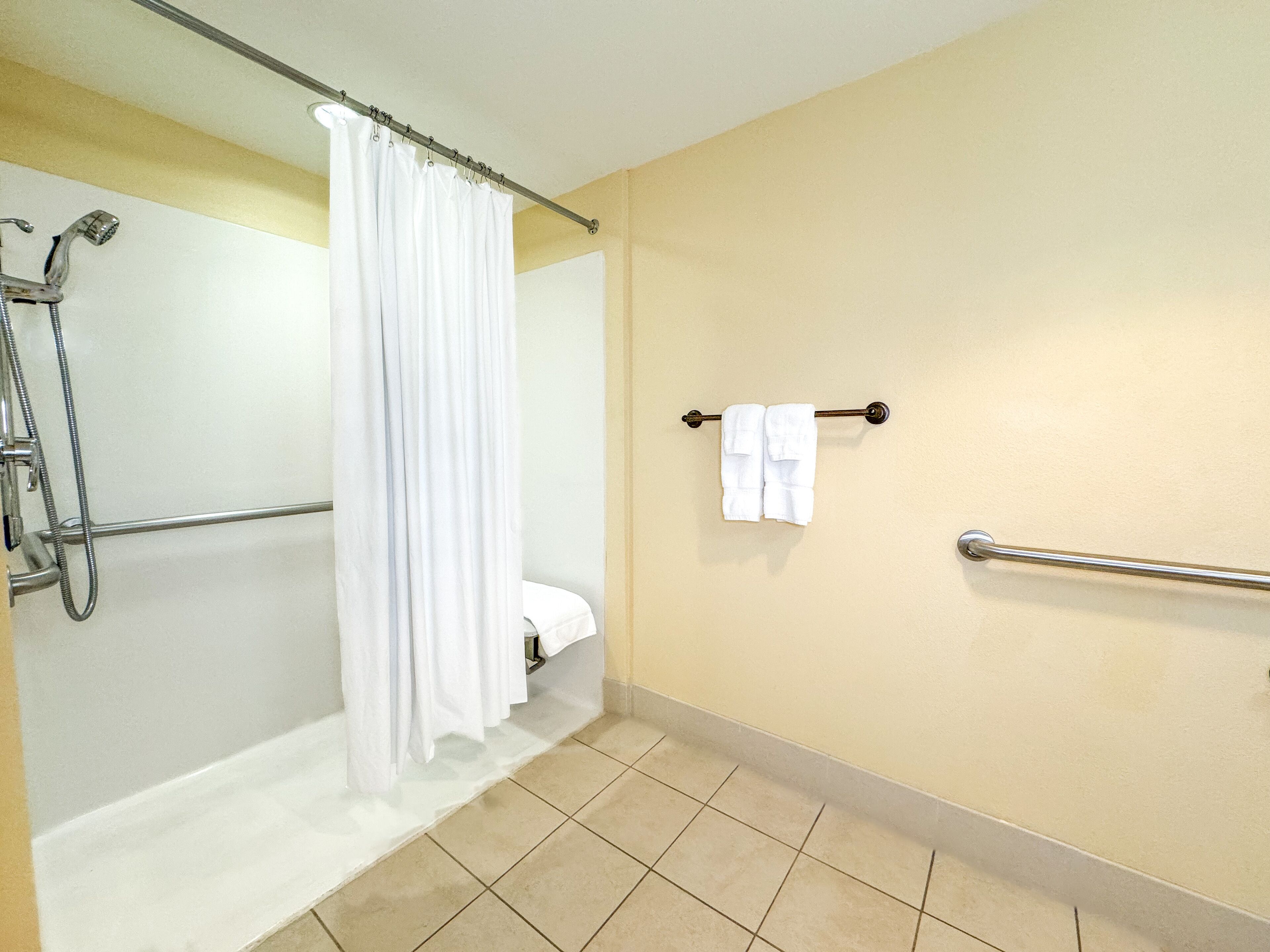 Un baño con ducha, inodoro y barras de apoyo.