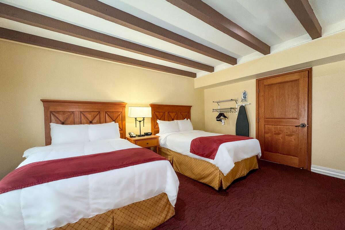 A hotel room with two beds, wooden headboards, a wooden door, and a wall-mounted ironing board.