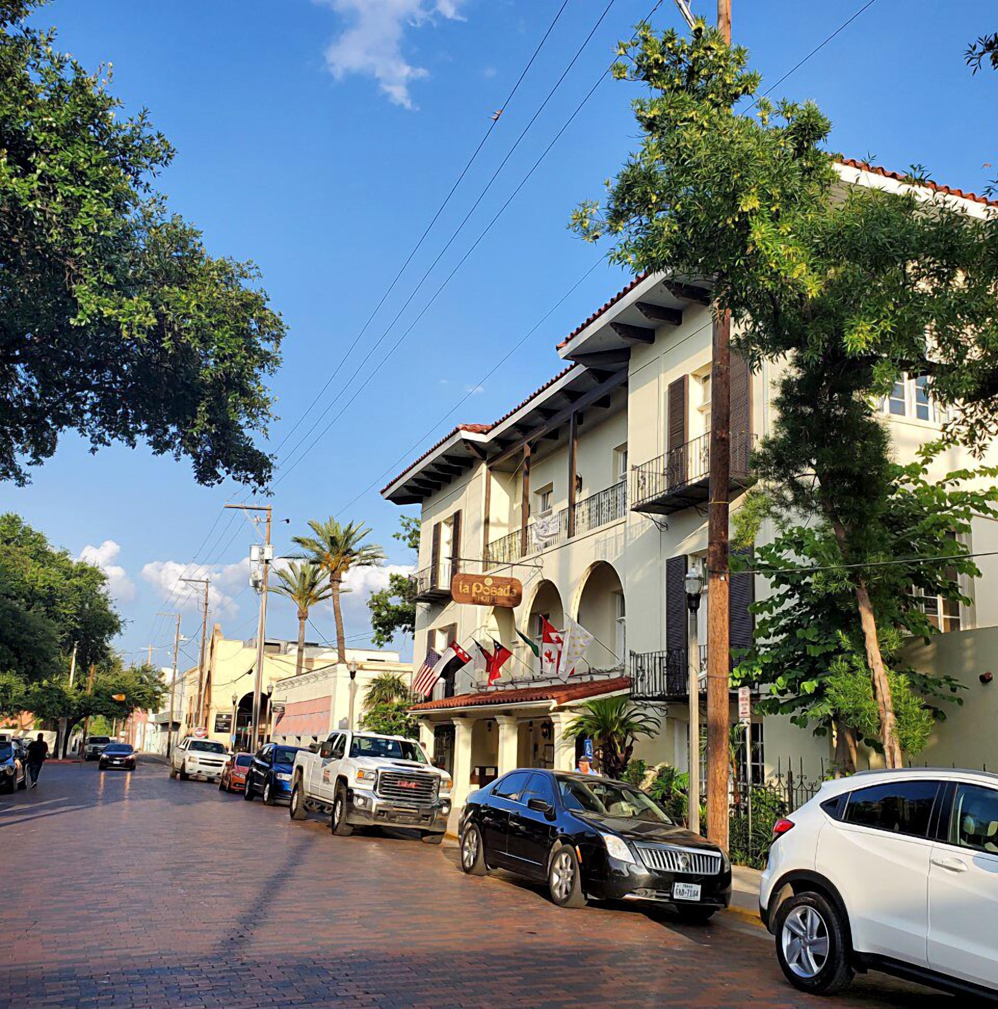 A hotel with a signboard, multiple balconies, and parked cars along a brick-paved street.