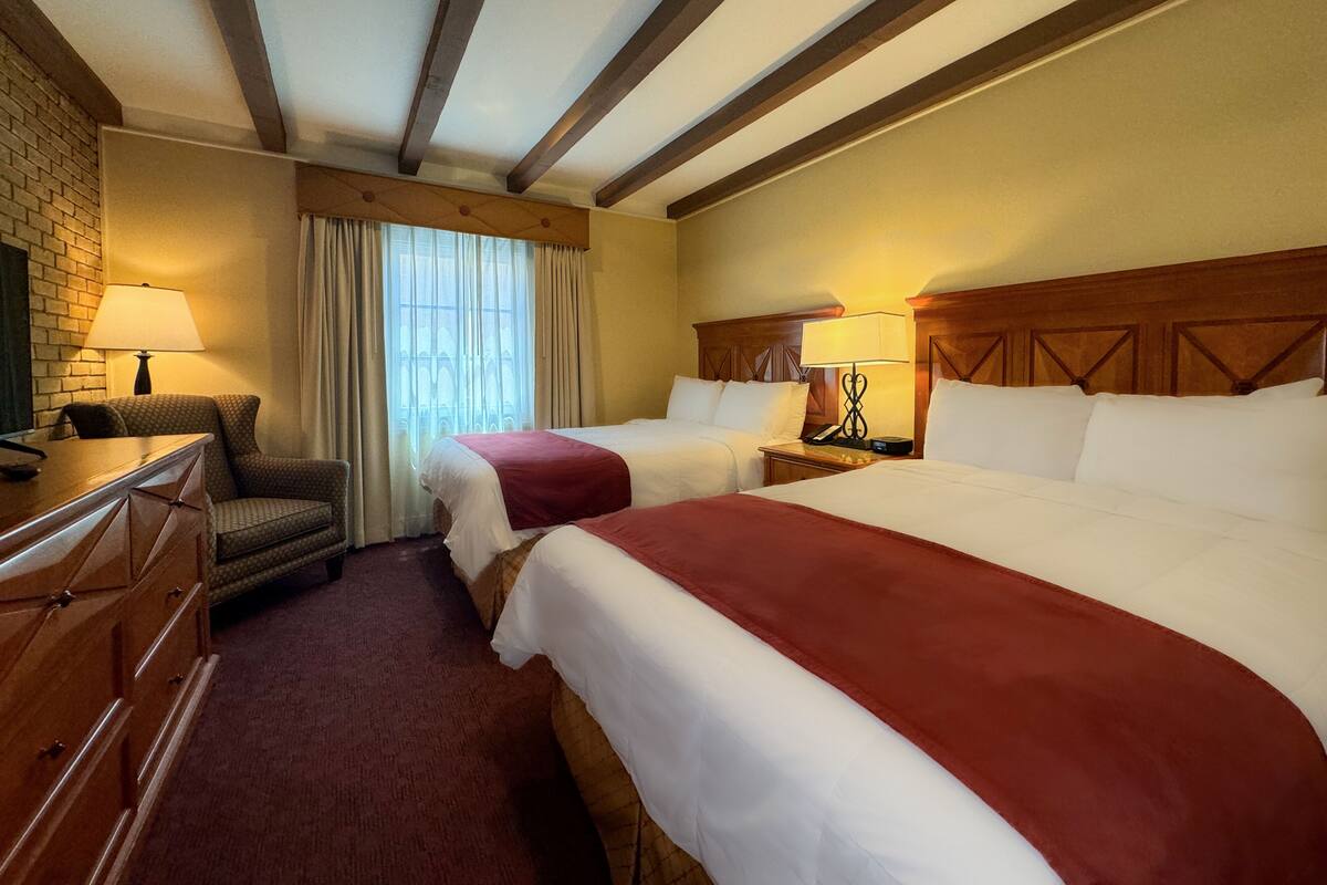 A hotel room with two beds, a desk, a chair, a lamp, and a window with curtains.