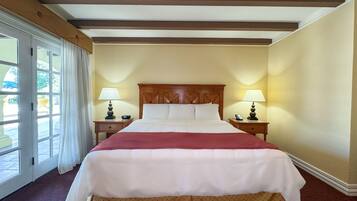 A large bed with a wooden headboard, two bedside tables with lamps, and a view of the outdoors through a glass door.