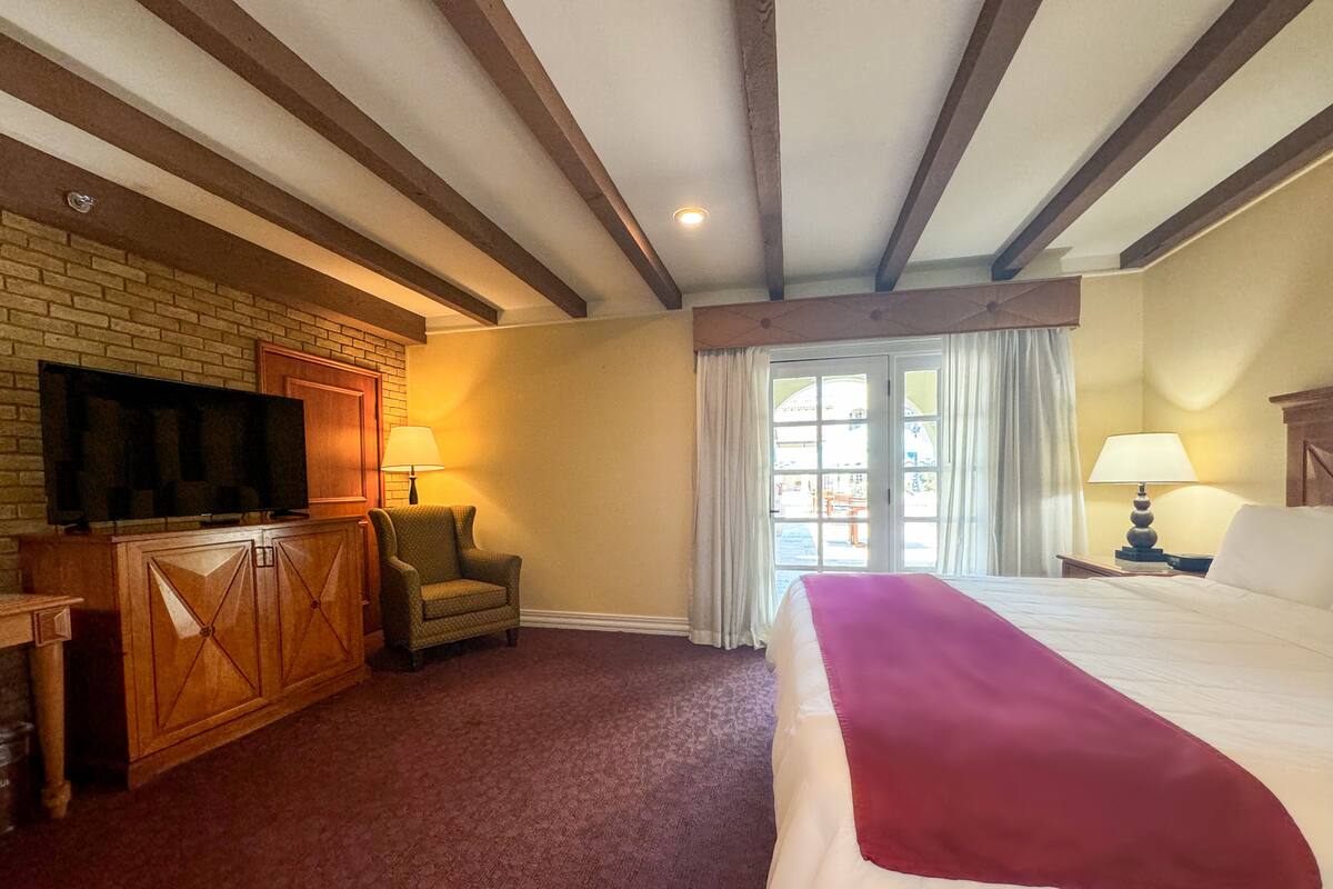 A hotel room with a large bed, a television on a wooden cabinet, a chair, and a window with curtains.