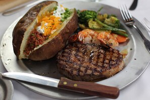 Un plato con un filete a la parrilla, una papa horneada cubierta con queso y crema agria, y verduras al vapor.