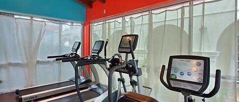 A gym with treadmills, an elliptical, and a stationary bike, featuring a wooden ceiling and large windows.
