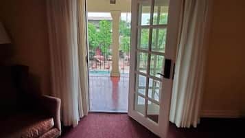 A hotel room with a red carpet, a sofa, a bed, and a view of a pool and greenery outside.