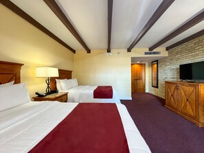 A hotel room with two beds, a TV, a wooden cabinet, and a brick wall.
