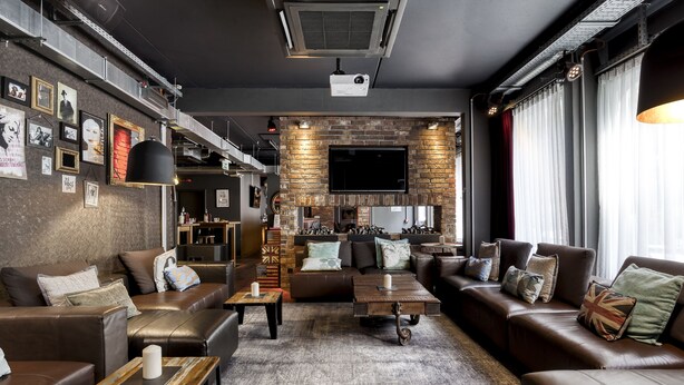 Een moderne woonkamer met leren banken, een open haard, een flatscreen televisie en een beamer.