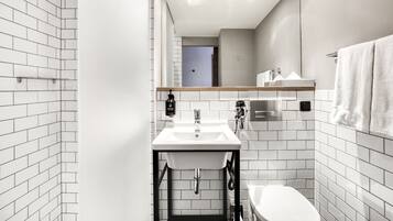 A modern bathroom with white subway tiles, a white sink, a toilet, and a mirror above the sink.