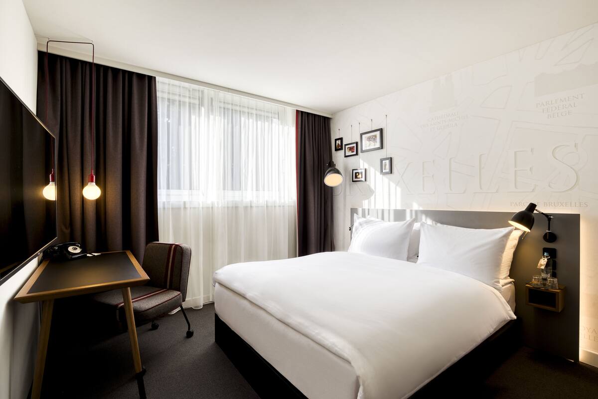 Une chambre d’hôtel avec un grand lit, un bureau, une chaise, une lampe et un mur orné de tableaux.