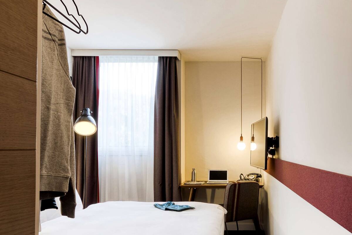 Une chambre d’hôtel avec un lit, un bureau, une chaise, un ordinateur portable et un miroir.