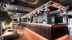 Een moderne bar met een lange toonbank, zitplaatsen en een grote plant.