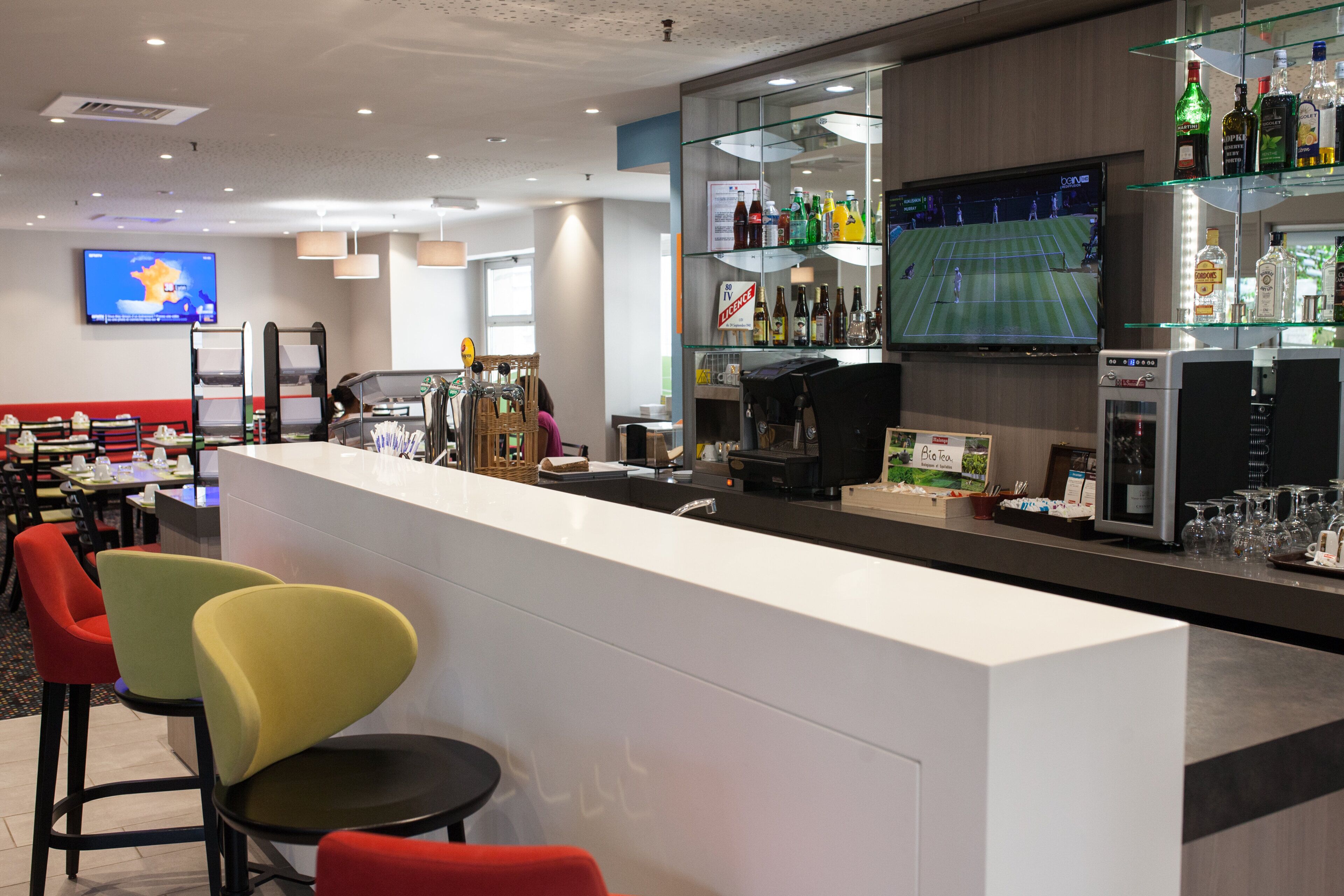 A bar area with seating, a television screen, and a variety of bottles and glasses.
