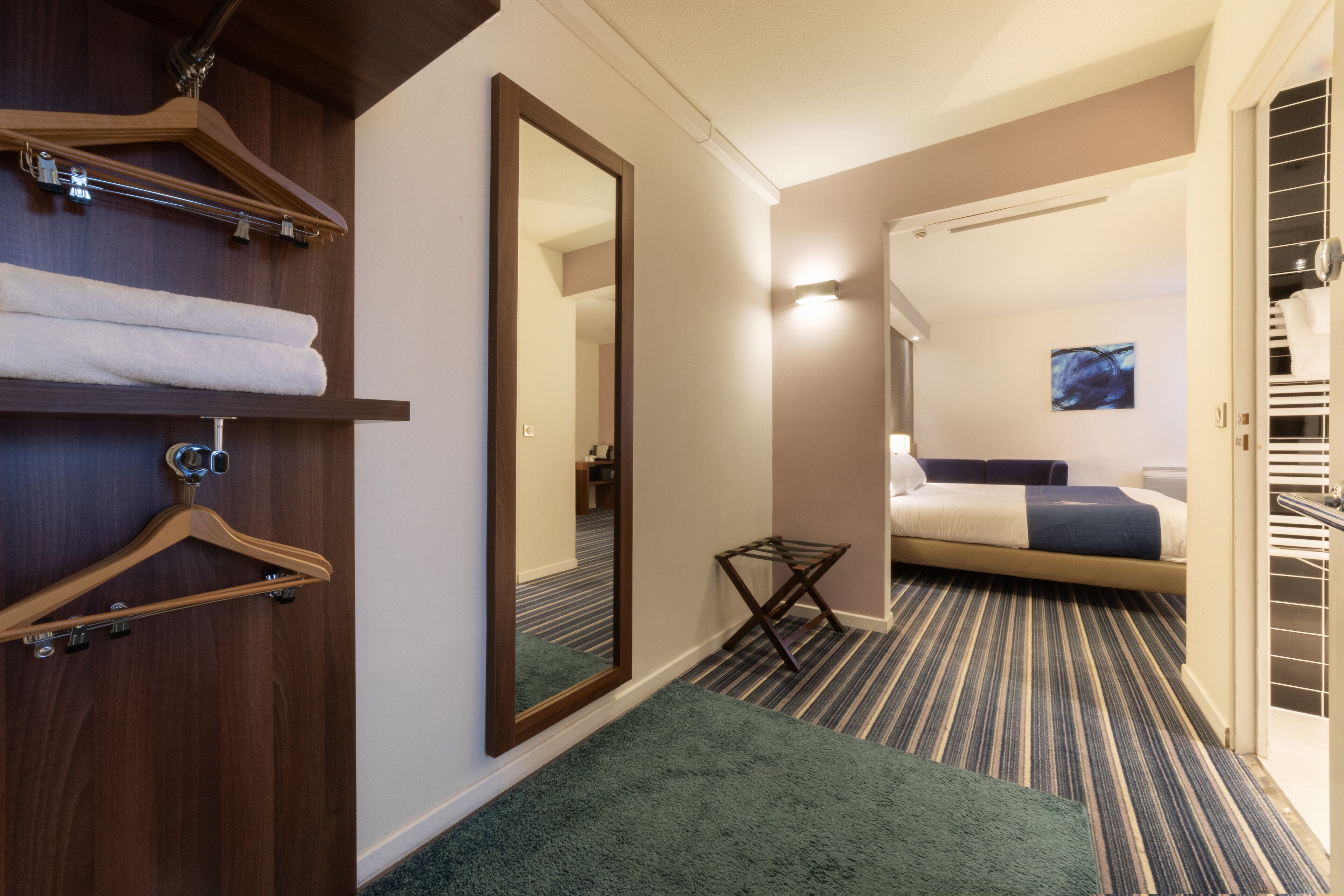 Ein Hotelzimmer mit einem großen Spiegel, einem Bett mit einem Streifenmuster-Teppich, einem kleinen Tisch und einem Kleiderschrank mit Kleidung.