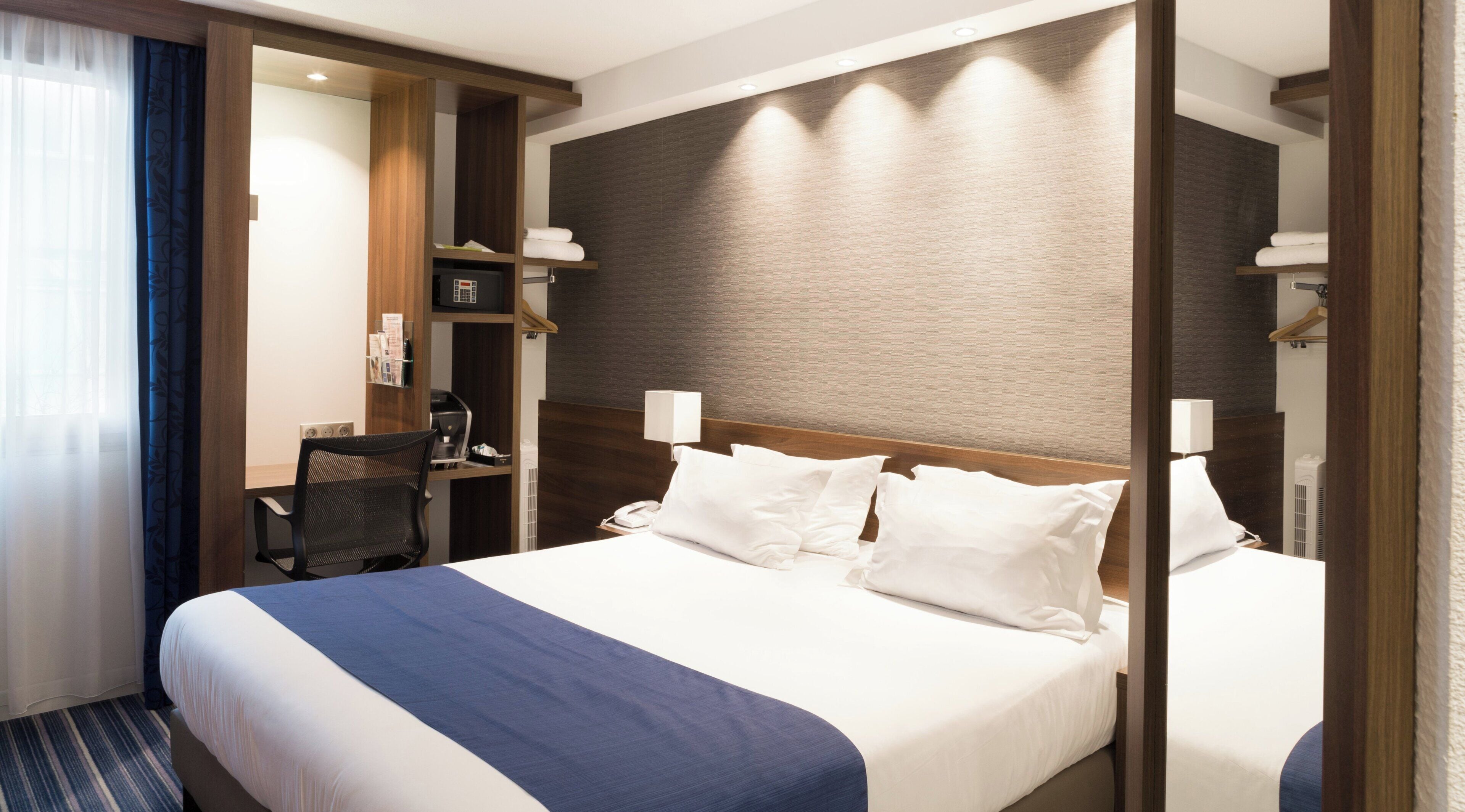 A hotel room with a large bed, a desk with a chair, a telephone, and a mirror.