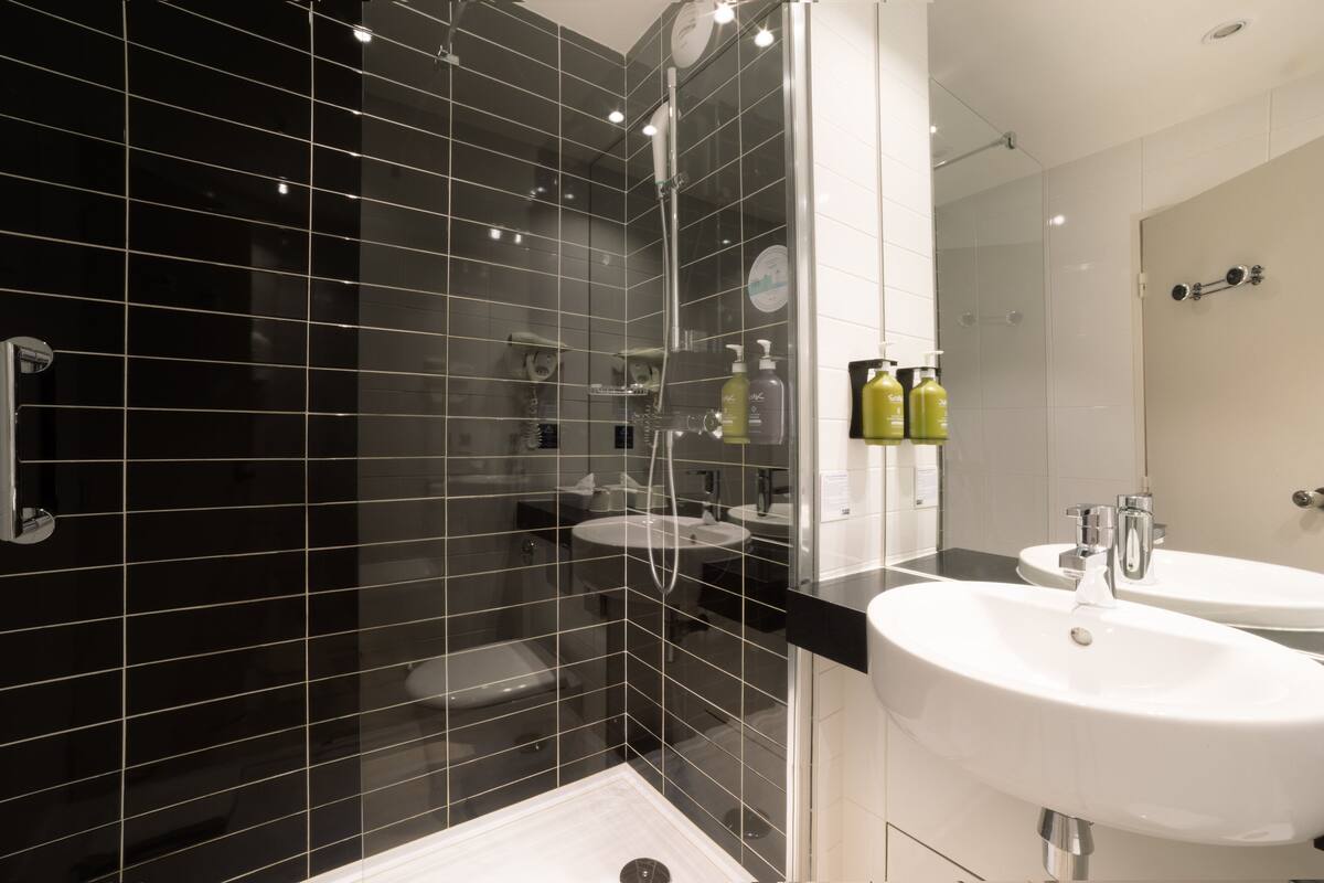 A modern bathroom with black tiled walls, a glass shower enclosure, and two white sinks with mirrors.
